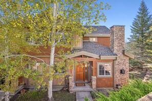 A two-story house with a stone chimney, a wooden front door, and a small porch.