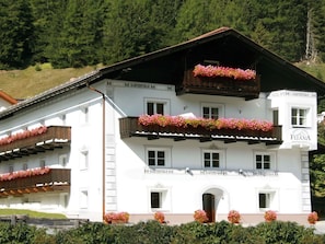 Un immeuble blanc doté de balcons ornés de fleurs roses, portant l’inscription « FLIANA APARTMENTS ».