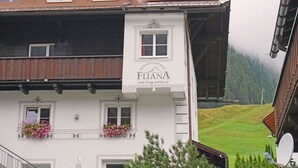 En bygning med et skilt, der viser 'FLANA APPAREMENTS', og en hjemmesideadresse. Den har flere vinduer og altaner med blomster.