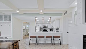 A modern kitchen with white cabinetry, a central island with stools, and a fireplace. - Starboard Village 612 | Beachfront | Pensacola Beach | Pool | My Beach Getaways (Pensacola Beach)