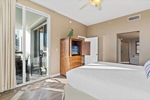 Een slaapkamer met een groot bed, een houten dressoir, een televisie en een schuifdeur naar een balkon.