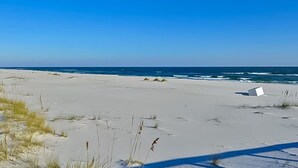 A sandy beach with a white structure, possibly a lifeguard tower, and the ocean in the background. - Spanish Key 307 | Beachfront | Steps from Flora Bama | Pools | My Beach Getaways (Pensacola)