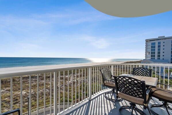 Een balkon met uitzicht op de oceaan, een tafel en stoelen, en een gebouw op de achtergrond.