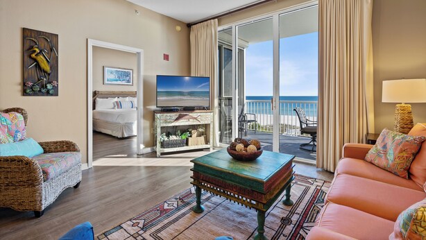 A spacious living room with a large television, a comfortable sofa, a coffee table, and a view of the ocean through a sliding glass door. - Spanish Key 307 | Beachfront | Steps from Flora Bama | Pools | My Beach Getaways (Pensacola)