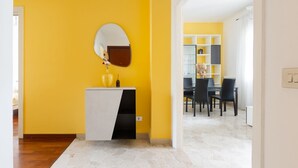 A room with a yellow wall, a white and black cabinet with a mirror, and a dining area with chairs and a table. - GuestHost - Milan Gambara Balcony Apartment (Milano)