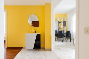 A room with a yellow wall, a white and black cabinet with a mirror, and a dining area with chairs and a table.