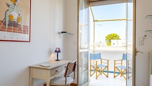Une pièce comprenant un bureau, une chaise, une lampe et une porte vitrée donnant sur un espace extérieur aménagé avec des chaises.