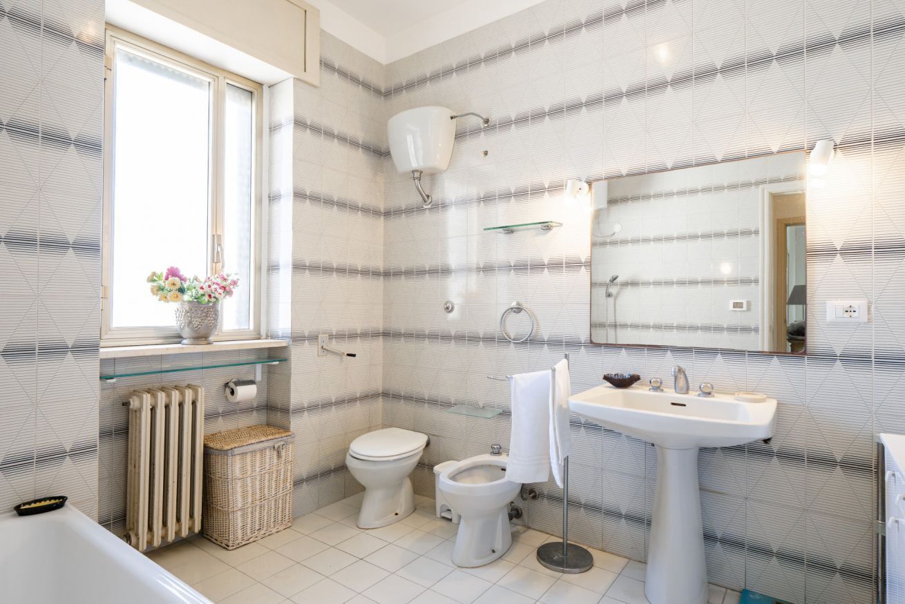 Une salle de bain comprenant des toilettes, un bidet, un lavabo et une fenêtre agrémentée d’un vase de fleurs.