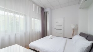 A modern hotel room with a bed, a desk, and a standing lamp.