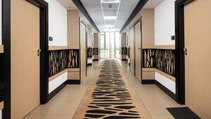 A hotel hallway with doors numbered 230 and 231, a patterned carpet, and a modern ceiling design.