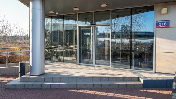 A modern building entrance with glass doors, a metal column, and a sign indicating the address.
