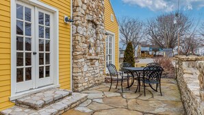 A yellow building with a stone wall and a stone patio with a table and chairs. - Charming Blake Cottage | Augusta Wine Country (Augusta)
