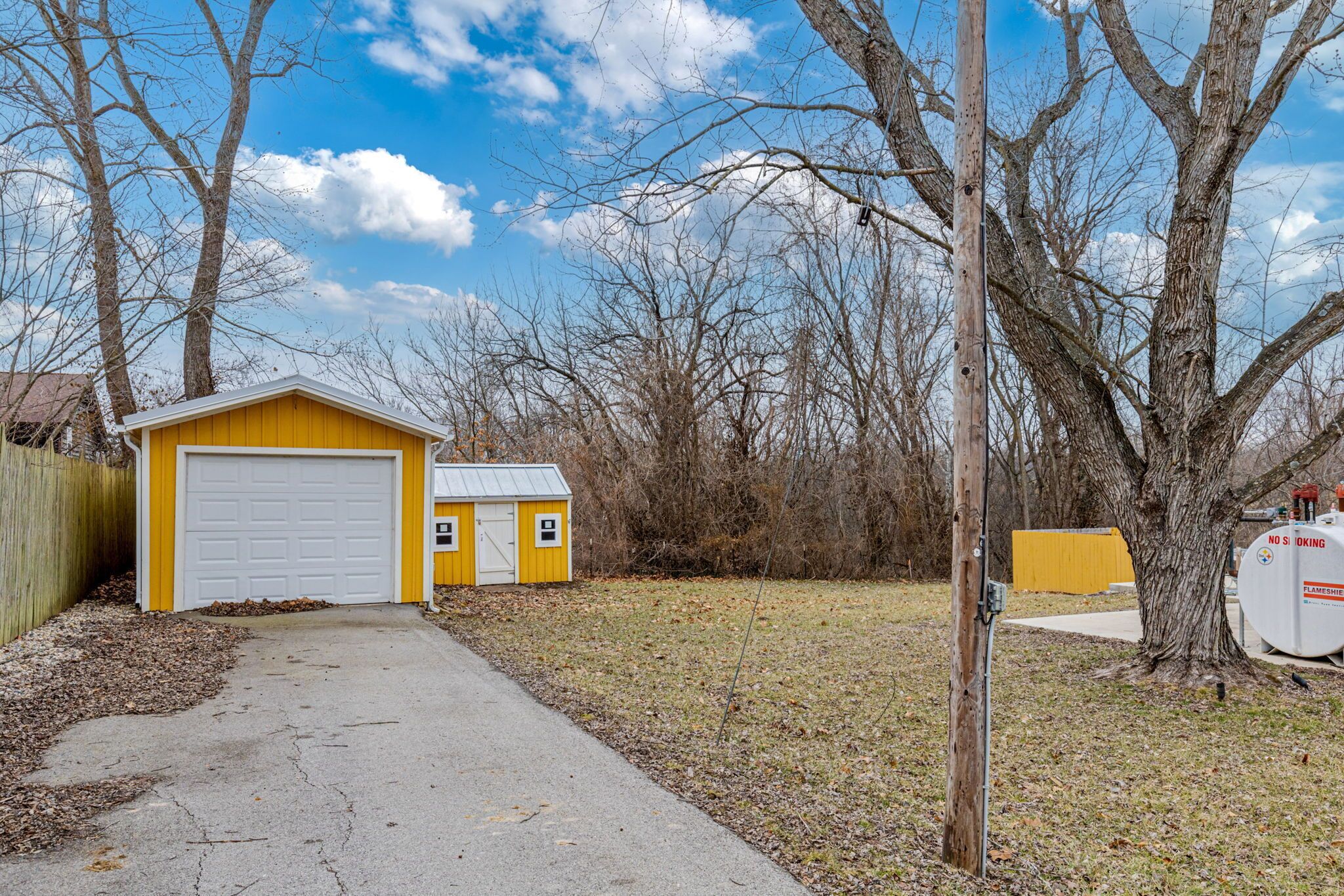 A yellow garage with a white door, a small shed, and a utility pole with a sign.