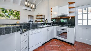 Una cocina con armarios blancos, encimera negra y suelo de baldosas.