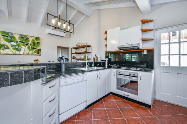 A kitchen with white cabinets, a black countertop, and a tiled floor. - Villa Martha - 3BR Villa (Paradera)