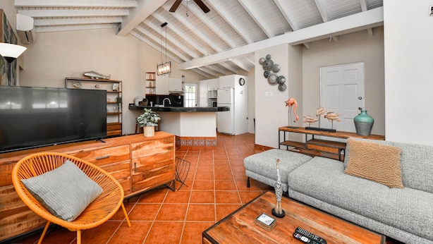 Amplia sala de estar con techo alto, televisor, sofá, mesa de comedor y cocina al fondo.