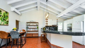 Una cocina con comedor, que cuenta con un techo alto, gabinetes blancos y piso de baldosas.