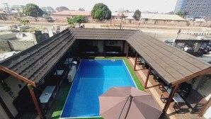 A rooftop swimming pool with blue water, surrounded by lounge chairs and an umbrella. - Muna Suites Owerri (Owerri)