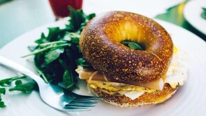A breakfast plate with a bagel sandwich, greens, and a fork. - Muna Suites Owerri (Owerri)