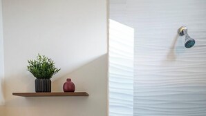 A bathroom with a toilet, shelves with decorative items, a towel rack, and a shower area with a towel rack. - Private Loft Cozy & Modern (San Luis Potosi)