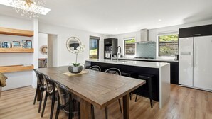 A modern kitchen with a central island, built-in appliances, and a dining area with a wooden table and chairs. - Sam`s Sanctuary | Stunning Views & Spacious Home (Queenstown)