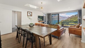 A modern living room with a wooden dining table, leather sofas, and a large window with a mountain view. - Sam`s Sanctuary | Stunning Views & Spacious Home (Queenstown)