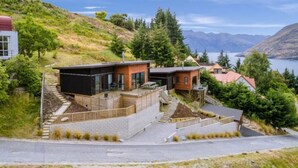 A modern house with a large deck, a stone pathway, and a view of a lake and mountains. - Sam`s Sanctuary | Stunning Views & Spacious Home (Queenstown)