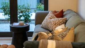A modern living room with a grey sofa, patterned cushions, and a small black side table with a book and a remote control. - Skippers Rest | Close to ski fields & parking (Queenstown)