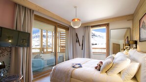 Une chambre à coucher avec un lit, une télévision, un bureau et une vue sur des montagnes enneigées, visible à travers de grandes fenêtres.