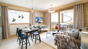 Ein modernes Wohnzimmer mit Essbereich, großen Fenstern und Blick auf eine Skipiste.