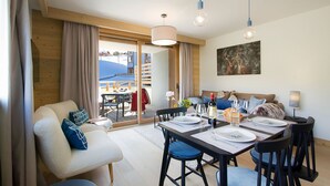 Ein modernes Wohnzimmer mit einer Couch, einem Esstisch für zwei Personen und einem Balkon mit Blick auf Gebäude.
