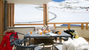 Ein Balkon mit einem Frühstückstisch, einem Stuhl und Blick auf eine verschneite Berglandschaft.