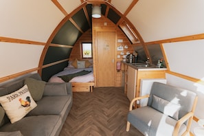 Une chambre confortable aménagée en mezzanine, avec un lit, un canapé, un fauteuil, un coin cuisine et une vue sur l’extérieur.