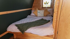 Un letto di legno con una coperta verde, cuscini rosa e una finestra vista fiori.
