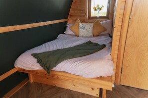 Una cama de madera con una manta verde, almohadas rosas y una ventana con vistas a flores.