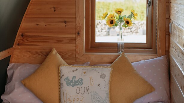 Um quarto aconchegante com teto de madeira, janela com vista para girassóis e cama com travesseiro com um pássaro e o texto 'this is our happy place'.