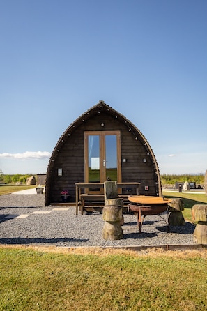 A wooden cabin with a large window, a wooden table, and a bench.
