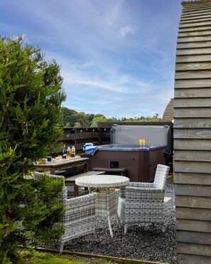 An outdoor patio with a hot tub, seating, and a table. - Cosy Modern Glamping Pod With Hot Tub (Newton Stewart)