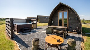 En rustik hytte med jacuzzi, træterrasse og et rundt bord.