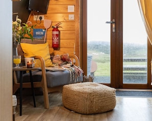 Una habitació acollidora amb interior de fusta, un llit amb llençol escocès, una taula petita amb una tassa i un got, i un extintor a la paret.
