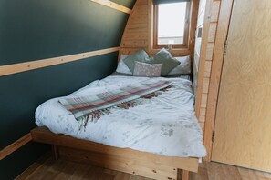 A bed with a wooden frame, a window above it, and a view of the outside.