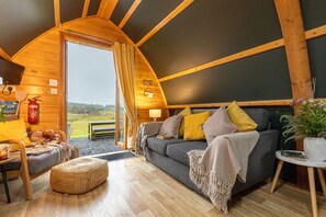 A cozy interior with a sofa, a small table, a chair, and a potted plant. - Cosy Modern Glamping Pod With Hot Tub (Newton Stewart)