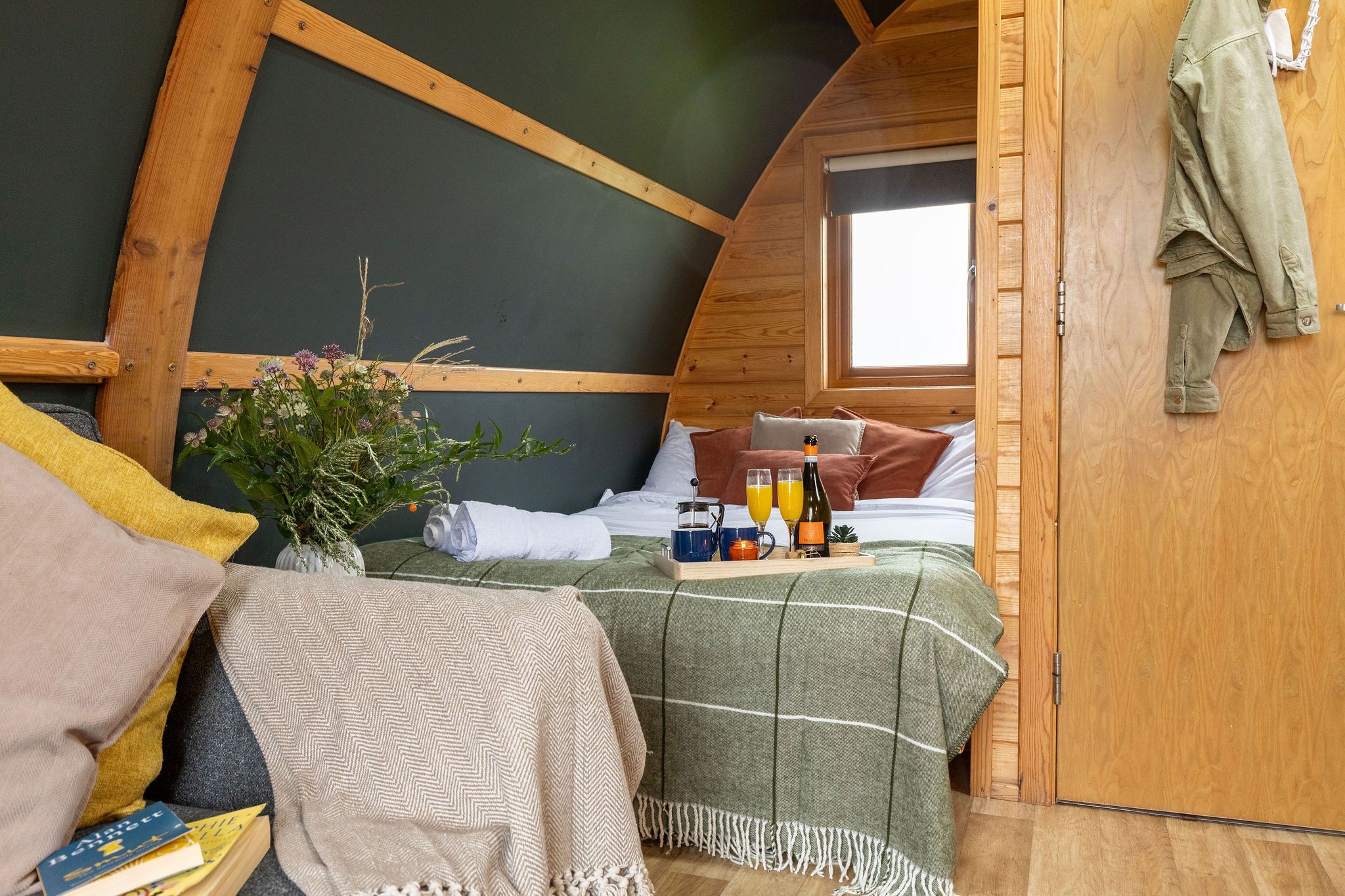 Un dormitorio acogedor en el ático con una cama, una mesita con bebidas y una botella, una ventana y una puerta de madera.