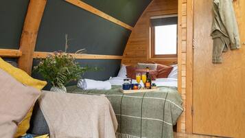 Un dormitorio acogedor en el ático con una cama, una mesita con bebidas y una botella, una ventana y una puerta de madera.