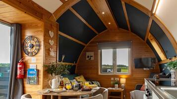 A cozy interior with a wooden ceiling, a dining area with chairs, a table with breakfast items, and a kitchen area.