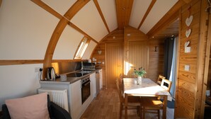 A cozy kitchen with wooden beams, a dining area with a table and chairs, and a small island with a kettle.