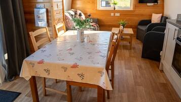 L’intérieur chaleureux d’un chalet avec une table à manger en bois, des chaises, un canapé et un téléviseur fixé au mur.