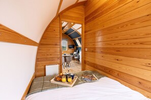 Une pièce chaleureuse aux murs lambrissés, avec un lit, un plateau de petit-déjeuner et une vue sur une autre pièce où se trouvent une table et des chaises.