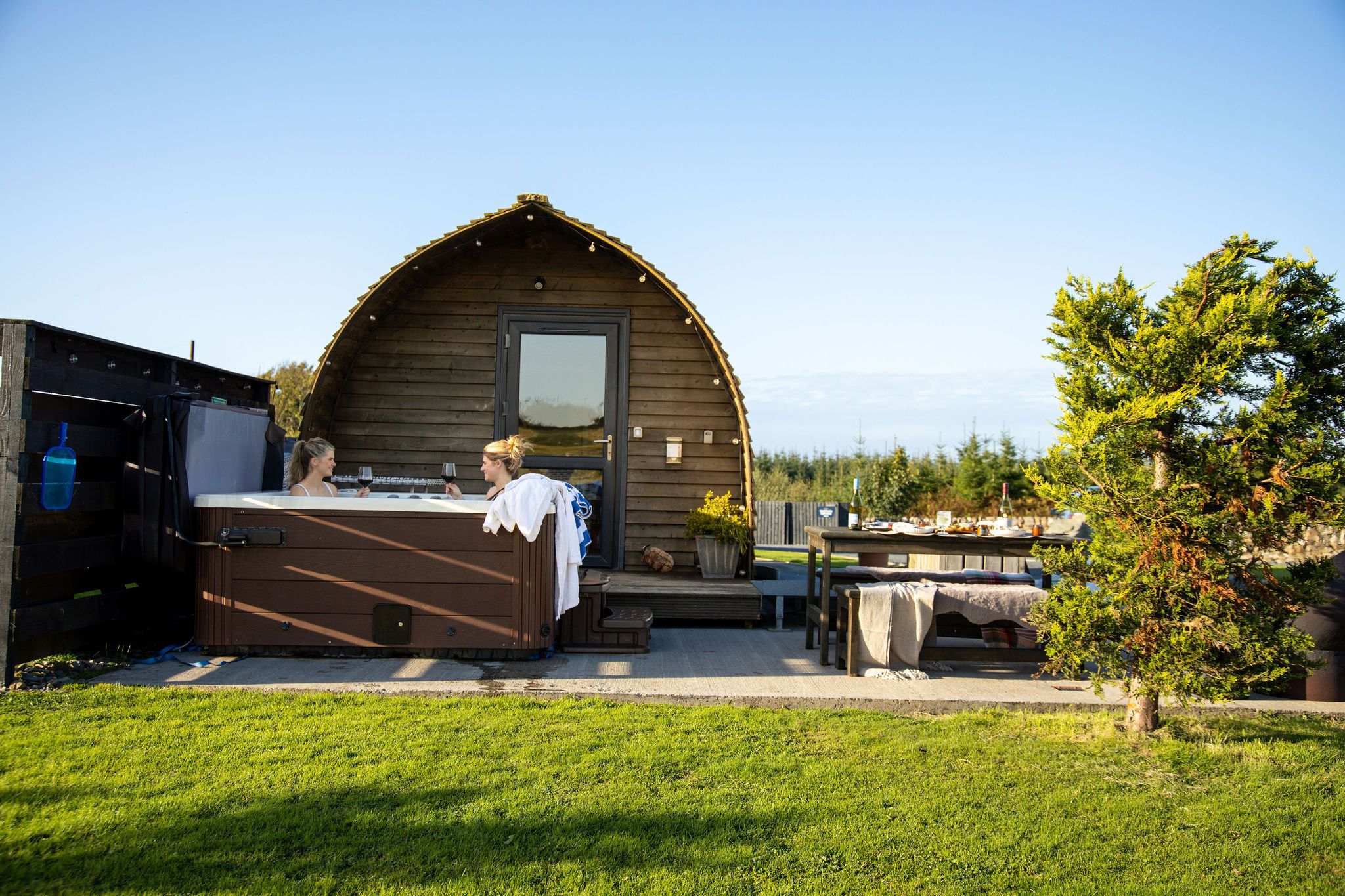Een houten chalet met een veranda, een eettafel gedekt voor twee personen en een kleine tuin.