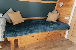 Ein kleines hölzernes Bett mit einer dunkelblauen Decke, zwei Kissen und einer herzförmigen Dekoration an der Wand.